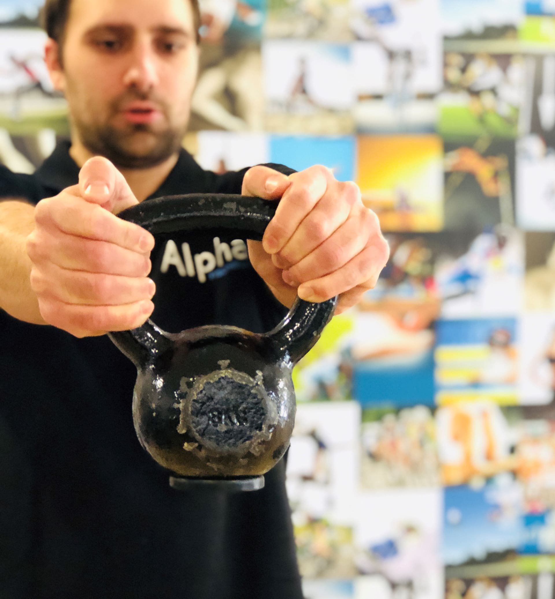 Trainer houdt een kettlebell met het Alpha-logo met twee handen vast